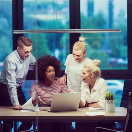 Group of business professionals gathered around a desk at TWIST IST, an audio visual company near me, attentively viewing a presentation on a laptop screen.